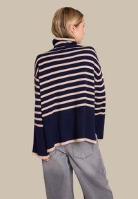 Marineblå og beige stripete høyhalset genser med avslappet passform, som har en bred, ribbestrikket hals og en senket søm. Mykt strikket stoff.