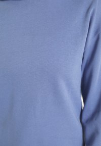 Ljusblå långärmad plagg gjort av mjukt tyg, har en slät yta och en rundad halsringning, med en avslappnad passform och inga synliga mönster.