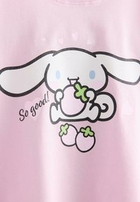 Hvid tegneseriekanin med blå øjne, der spiser en pink frugt, omgivet af tre flere pink frugter på en lyserød baggrund med teksten "Så godt!".