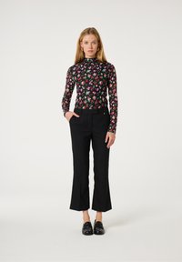 Zwarte bloemen lange mouwen top met meerkleurige patronen, gecombineerd met zwarte op maat gemaakte broeken. Model staat in zwarte loafers, met de handen in de zakken.