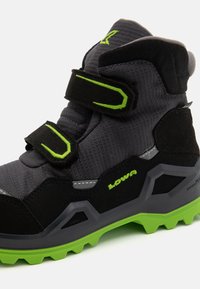 Black and gray hiking boot with green accents, featuring a textured upper, Velcro straps, and a durable rubber outsole with traction lugs.