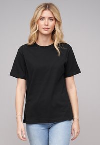 Black cotton t-shirt with short sleeves and a crew neckline. Worn with light blue jeans, featuring a casual fit and smooth texture.