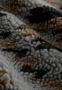 Strukturiertes Gewebe in Grau, Schwarz und Braun mit einer weichen, flauschigen Oberfläche, die ein Muster aus verschiedenen Formen und Farben aufweist.