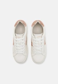 White sneakers with a smooth finish, featuring a rose gold shimmery accent and white laces. The interior shows a light gray lining with branding.
