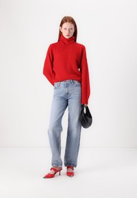 Crvena pletena turtleneck pulover, širokog kroja; svijetloplave traperice; crna torba; crvene cipele s visokom petom i srebrnim detaljima.
