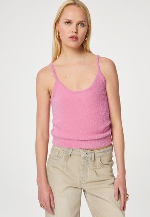 Flauschiges pinkes Tanktop mit dünnen Trägern und einem runden Ausschnitt, kombiniert mit hellbeigen, hochgeschnittenen Hosen. Der Stoff hat eine weiche Textur.