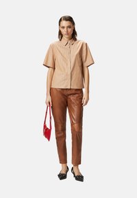 Camicia a maniche corte a righe marroni, pantaloni in pelle marrone a sigaretta, décolleté nere a punta, mentre tiene una piccola borsa rossa.