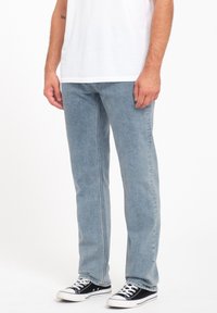 Jean en denim bleu clair avec une coupe droite, des détails de couture et un design à cinq poches, associés à des baskets en toile noires.