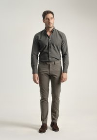 Camisa de botón verde oscuro, pantalones ajustados verde claro, zapatos de ante marrón; textura suave, diseño a medida, silueta entallada.