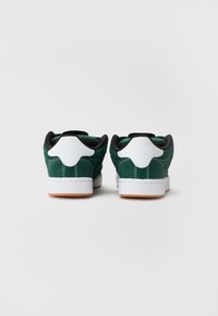 Baskets basses en suédine verte avec des accents noirs, un tab heel blanc et une semelle en caoutchouc gomme. Présente des détails cousus sur les côtés.
