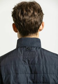 Marinblå puffjacka med hög krage, kviltat mönster och en knappdetalj på baksidan. Slät tyg med horisontell sömnad.