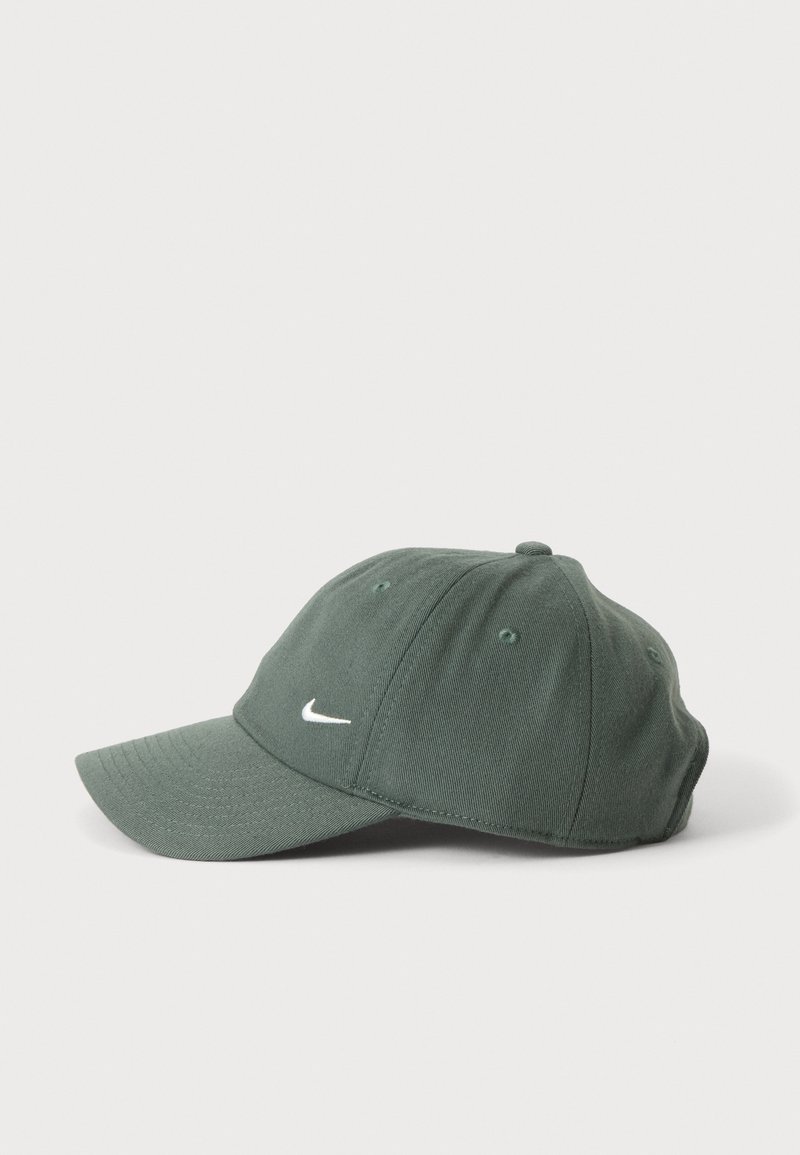 Mørkegrøn baseballcap med et lille hvidt swoosh-logo foran, vist fra siden på en ensartet lys grå baggrund.