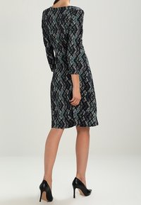 Svart klänning med ett flerfärgat geometriskt mönster, långärmad, figursydd liv och utsvängd kjol, kombinerad med svarta högklackade skor.