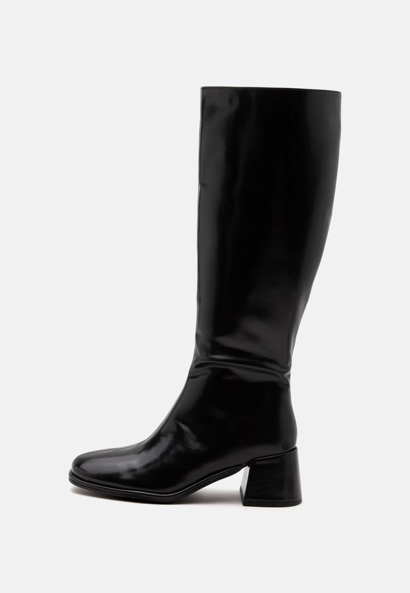 Botte en cuir noire brillante jusqu'au genou, avec un bout arrondi et un petit talon bloc, vue de côté sur un fond uni.