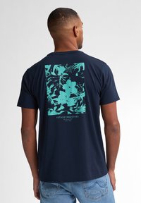 T-shirt marine avec un graphique floral turquoise au dos, en coton doux, col rond et manches courtes.