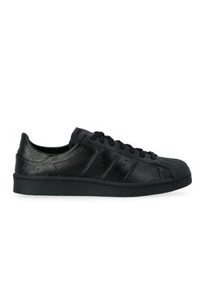 Sneaker nera bassa con lacci, punta testurizzata, strisce laterali perforate e logo in rilievo discreto sul tallone.