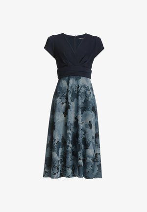 Abito blu navy con maniche a cappuccio, caratterizzato da un corpetto aderente e una gonna svasata plissettata decorata con un motivo astratto blu e nero. Cerniera sul retro.