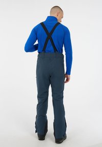 Technische skibroek gemaakt van donkerblauwe stof met zwarte verstelbare bretels en ritsen aan de zijkant. Draagt met een blauwe lange mouwen top.