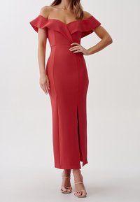 Rød off-the-shoulder kjole med voluminøse ærmer, tætsiddende silhuet, knæhøj slids og struktureret stof. Klare, glatte linjer fremhæver designet.