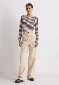 Pasiasty, długi rękaw top w kolorze brązowym i kremowym, w połączeniu z beżowymi, wysokimi na biodrach spodniami z korduroy o szerokich nogawkach, teksturowanymi prążkowanym wzorem i dwoma guzikami.