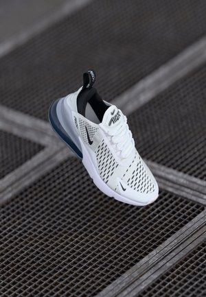 Hvid Nike Air Max sneaker med sorte detaljer og synlig luftpolstring, vist over en metalrist gulvflade.