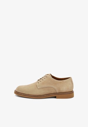 Zapato de vestir de hombre beige de gamuza con cordones, suela de goma marrón y detalles de costura, mostrado de lado sobre un fondo blanco.