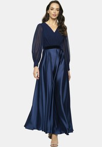 Granatowa satynowa długa sukienka z dekoltem w szpic, przezroczystymi długimi rękawami i dopasowanym gorsetem. Charakteryzuje się zwiewną spódnicą i aksamitem zdobionym pasem w talii.