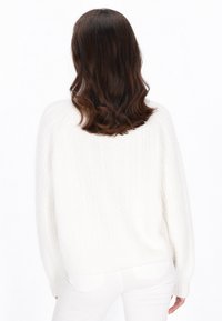 Weißer Strickpullover mit entspannter Passform, der ein strukturiertes Rippmuster und herunterfallende Schulternähte aufweist, kombiniert mit weißen Jeans.