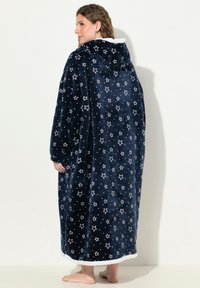 Coperta con cappuccio di colore blu navy con motivo a stelle bianche, in tessuto morbido, design lungo che arriva fino alle caviglie, bordatura bianca lungo il margine inferiore.