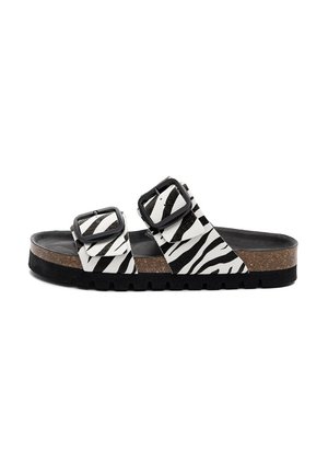 Sandał na slajdzie z czarno-białymi paskami w wzór zebry, dwoma czarnymi klamrami, korkową wkładką i grubą czarną gumową podeszwą.