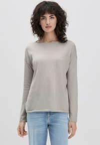 Helles graues Langarmshirt aus weichem Stoff, mit weitem Ausschnitt und lässigem Schnitt, kombiniert mit hellblauen Jeans.