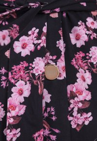 Zwarte stof met een bloemenprint van roze bloemen. Inclusief een gouden knop met de tekst "BIZUU". Geplooide textuur langs het ontwerp.