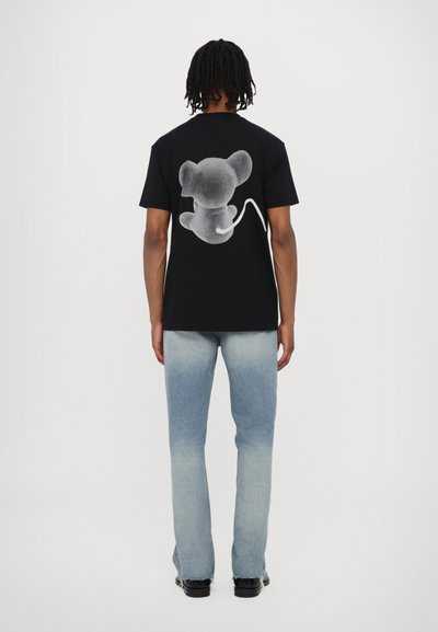 Black short-sleeve t-shirt featuring a gray graphic of a cartoon mouse on the back. Paired with light denim jeans and black shoes.