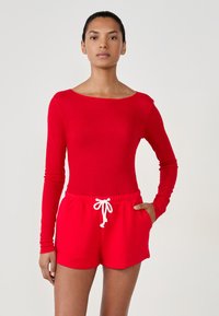 Haut à manches longues côtelé rouge, associé à un short rouge avec taille à cordon et poches latérales, mettant en valeur une texture lisse et une couleur vive.