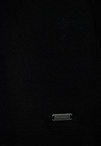 Tissu tricoté noir avec une petite étiquette de marque métallique "nümph" cousue près du bord inférieur.