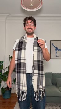 Sivorjastek in beli škripavi šal s resicami, narejen iz mehkega materiala, nosi oseba, ki ga ima ovitega okoli ramen.