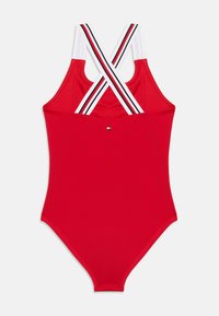 Κόκκινο ολόσωμο μαγιό με σταυρωτούς λευκούς, μαύρους και κόκκινους ριγέ ιμάντες και ένα μικρό λογότυπο στο κέντρο της πλάτης.