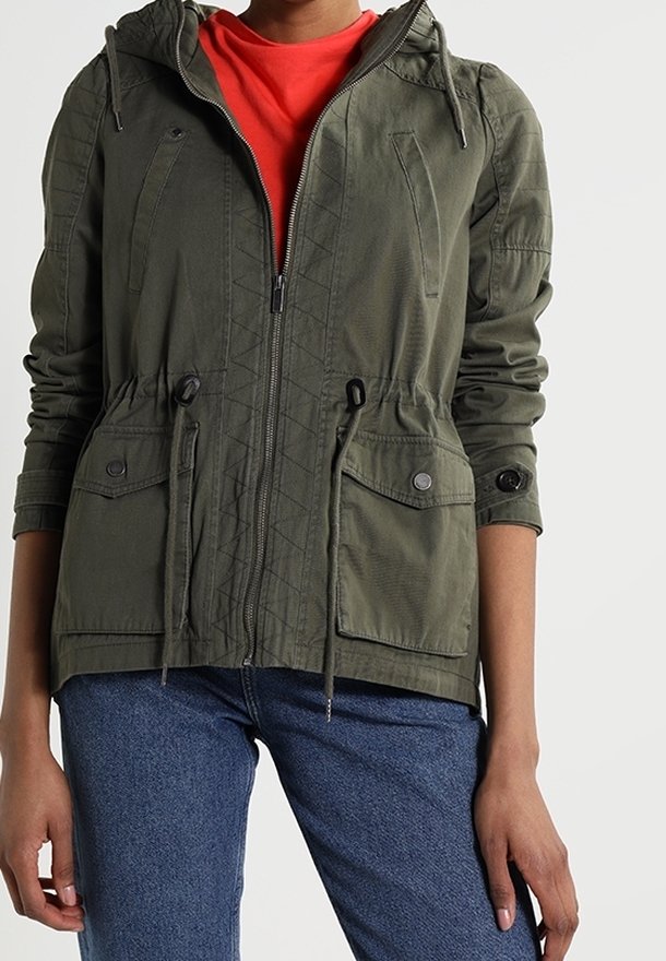 Olivgrön zip-up jacka med huva, dragsko i midjan, två framfickor och texturerade sömnadsdetaljer, kombinerad med en röd skjorta under.