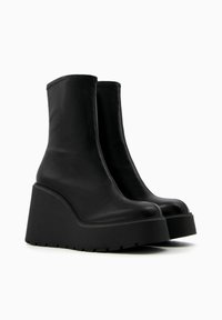 Black, leather ankle boots with a high wedge heel, rounded toe, and smooth texture. Features a thick rubber sole with a patterned tread.