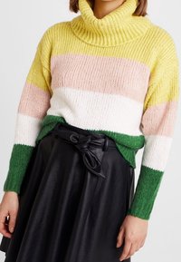 Gruba sweter typu golf z poziomymi paskami w kolorach żółtym, różowym, białym i zielonym; noszony na tle czarnej skórzanej spódnicy o wysokim stanie.