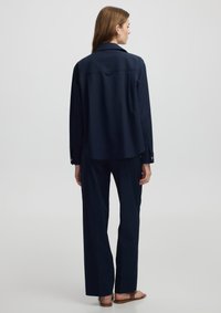 Navyblauwe, lange mouwen shirt met kraag, met een ontspannen pasvorm en knoopdetails, gecombineerd met losse navybroeken.