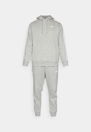 Set felpa e pantaloni grigi realizzati in tessuto morbido. La felpa presenta una tasca frontale e un logo, mentre i pantaloni hanno polsini elasticizzati e dettagli con il logo.