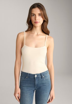 Débardeur beige à fines bretelles et décolleté carré, associé à un jean en denim bleu ajusté. Texture lisse, design décontracté.