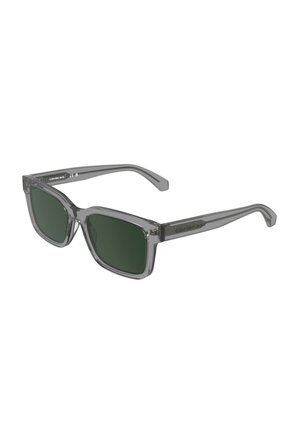 Lunettes de soleil rectangulaires avec des verres vert foncé et des montures et branches grises transparentes, marquées Calvin Klein Jeans sur les branches.