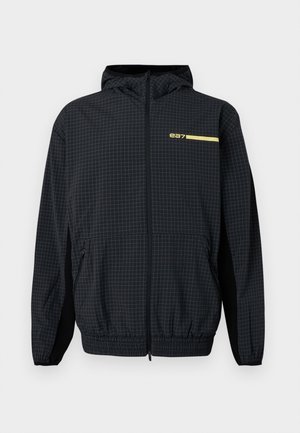 Črna jakna s kapuco s subtilnim vzorcem mreže, z zadrgo po celotni sprednji strani, elastičnim robom in manšetami, žepki na straneh z zadrgo ter majhnim rumenim logotipom "ea7" na prsih.