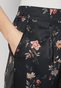 Pantaloni in satin nero con stampa floreale in rosa, arancione e verde. Presentano plissettature e tasche laterali, offrendo una texture liscia e una vita aderente.
