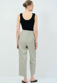 Černý bezrukávový bodysuit spárovaný s světle šedými kalhotami s elastickým pasem, které mají volný střih a rovný střih nohavic. Černé nazouvací boty.