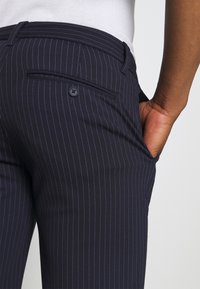 Námořnické kalhoty s jemným proužkem vyrobené z hladké tkaniny se slim fit střihem, obsahující zadní kapsu a zapínání na knoflík.
