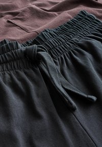 Sorte sweatpants med en samlet elastikliv, der har snørre. Blød tekstur, med en lomme på det mørkerøde øverste lag ovenfor.