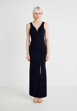 Robe maxi bleu marine avec un décolleté en V profond et une fente sur le côté, fabriquée dans un tissu lisse. Présente des bretelles larges et une silhouette ajustée, sans motifs.